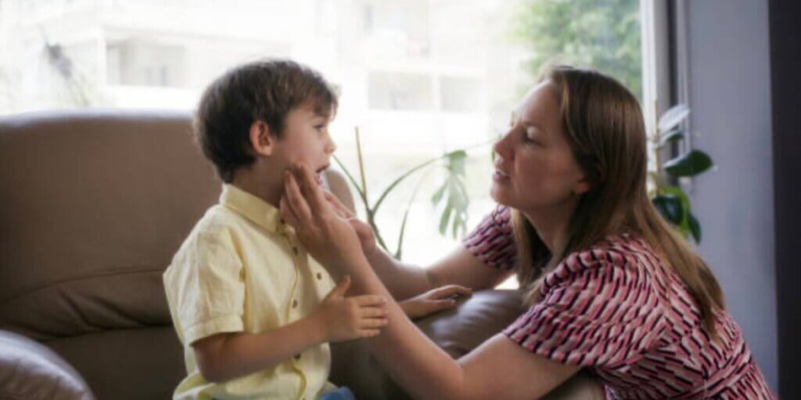 A mother looking into her child's mouth as he sits on a chair in an office