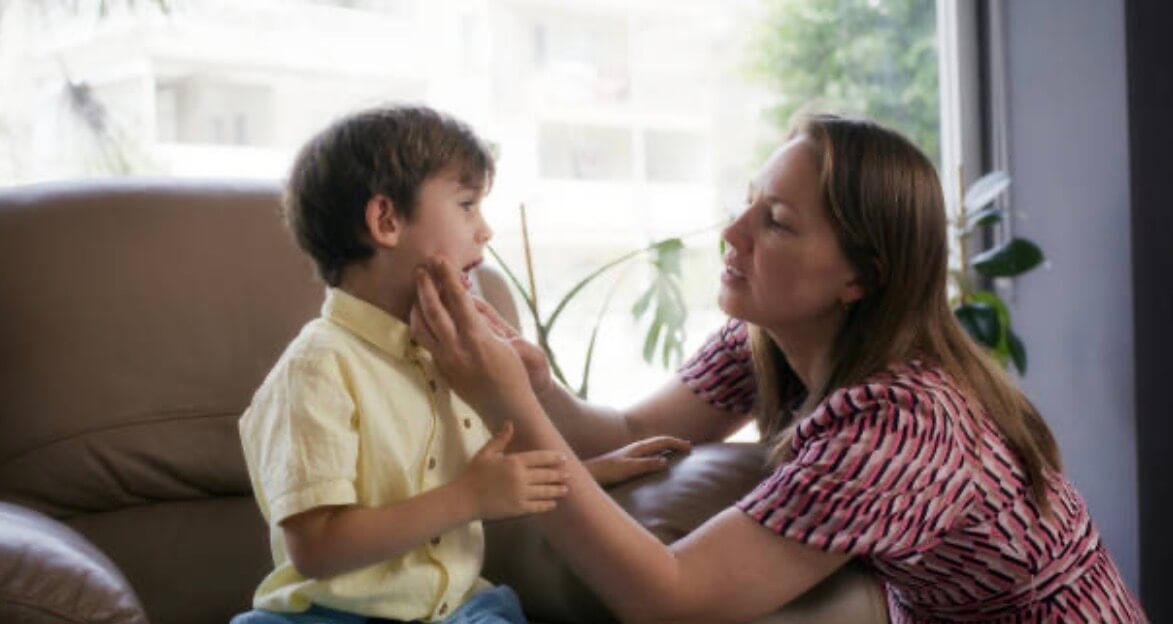 A mother looking into her child's mouth as he sits on a chair in an office